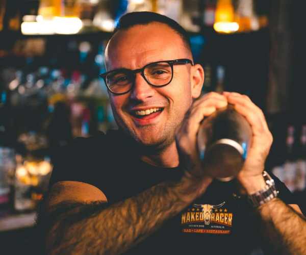 Un barman che agita un cocktail sorridendo a Naked Racer 